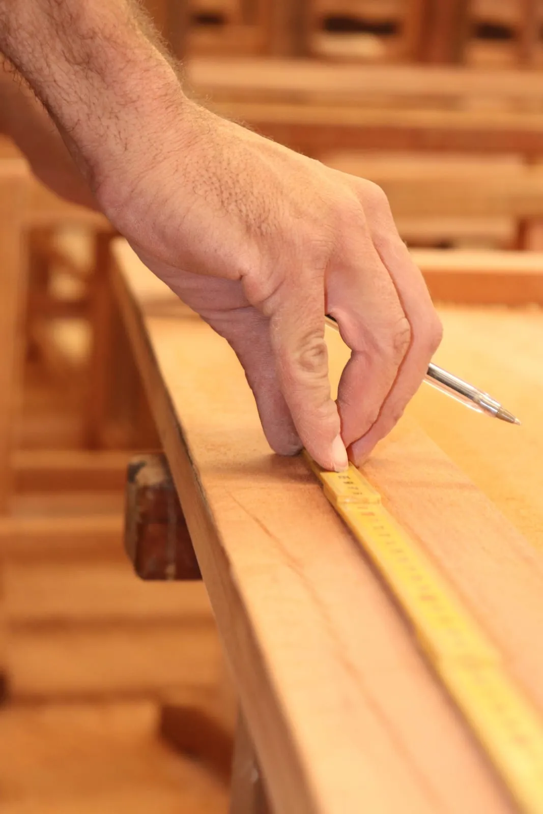 Schreiner vermisst einen Holzbalken mit Zollstock und Bleistift in der Werkstatt
